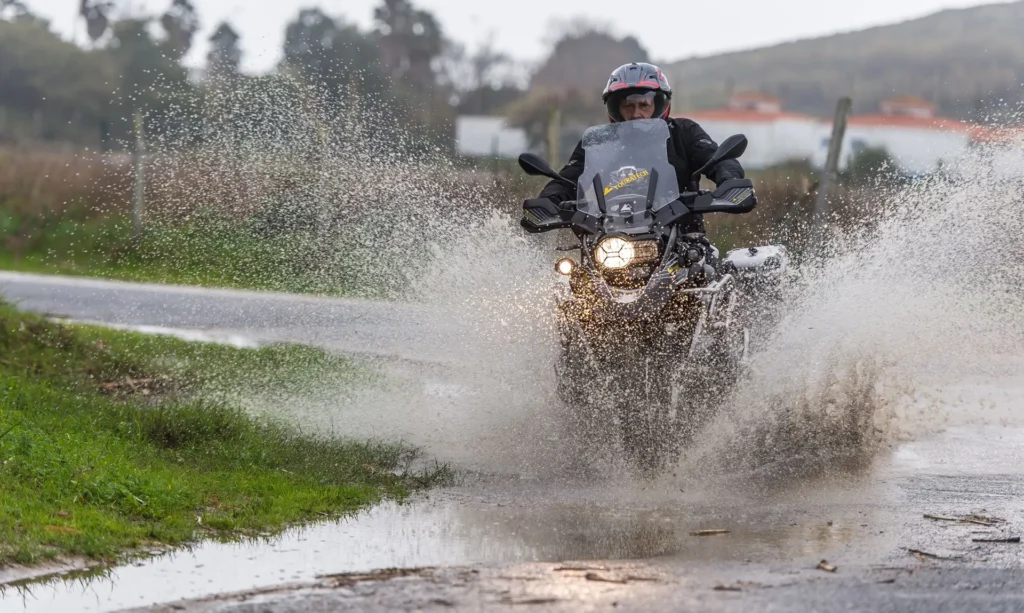 Motociclista com jaqueta impermeável pilotando uma moto em uma estrada sob forte chuva.