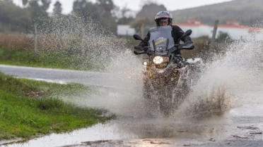 Motociclista com jaqueta impermeável pilotando uma moto em uma estrada sob forte chuva.
